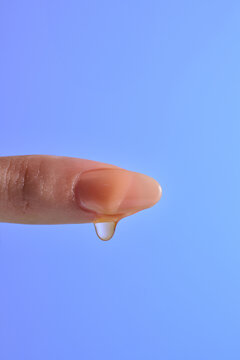 A single drop of liquid forming on the tip of a human finger