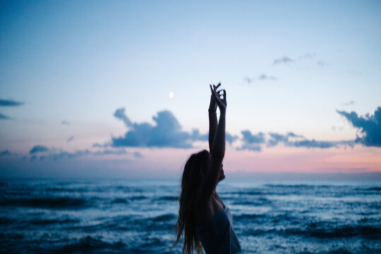 Woman raising arms beside ocean at blue hour