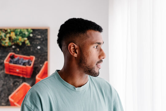 Modern Black man, gazing thoughtfully out the window of his apartment