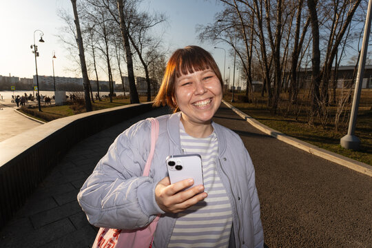 Woman Laughing Holding Smartphone in Sunny Urban Riverside Park