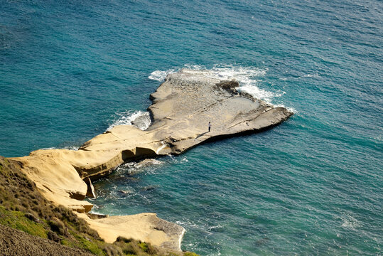 Lone figure on rocky plateau surrounded by vast sea
