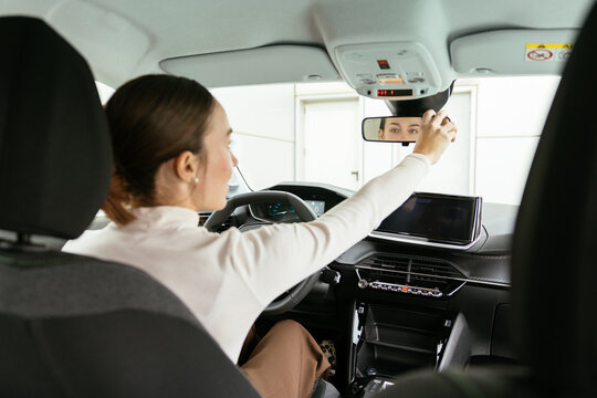 Woman adjusting rearview mirror in charging electric car