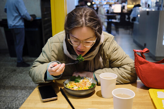 Woman eating a bowl of food at a table during lunch