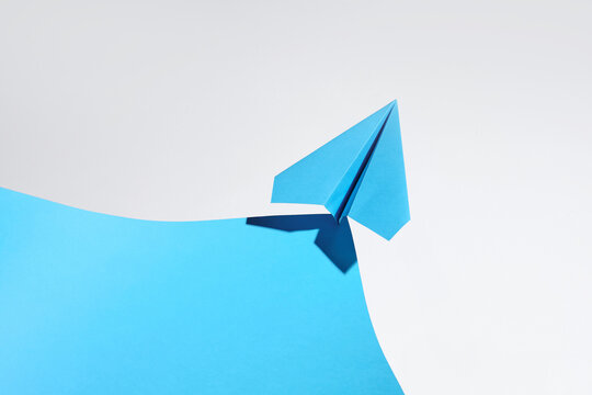 Blue paper airplane takes flight from a curved blue surface
