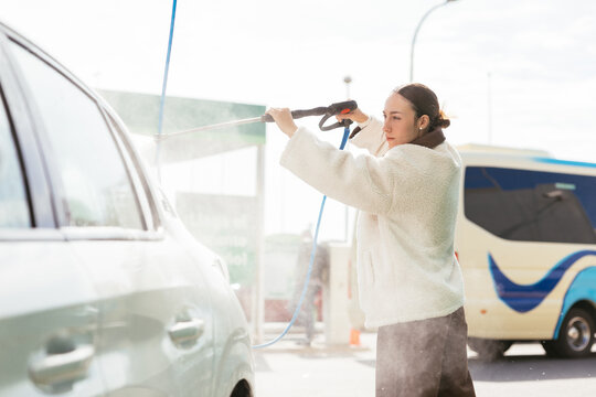Woman washing private car with high pressure cleaner