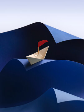 Origami paper boat with red flag sailing on abstract blue waves