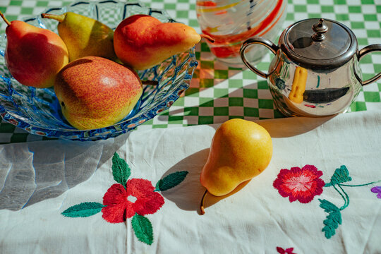 Fresh pears on table with floral cloth and teapot in morning light