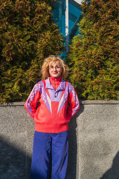 Woman in colorful retro sweater standing outdoors by greenery