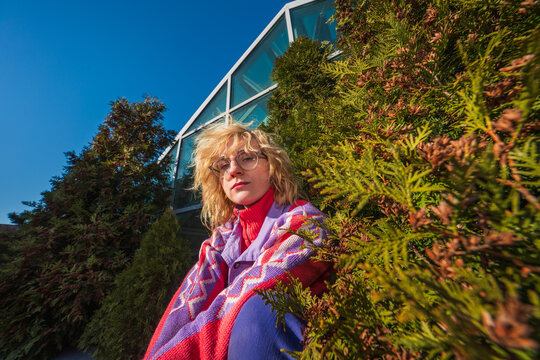 Woman in colorful sweater sitting by greenery and glass building