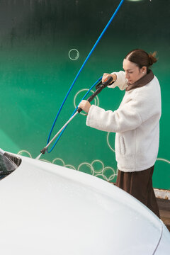 Woman washing white car with pressure washer