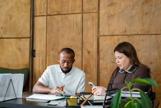 Multiracial colleagues look at their phones in office.