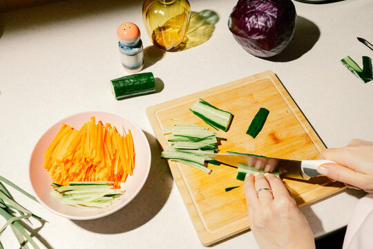 Young woman chopping cucumber salad for dinner.