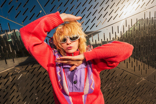 Woman in sunglasses posing playfully against metal wall
