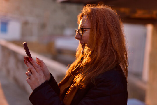 Smiling woman with orange hair using phone in warm light