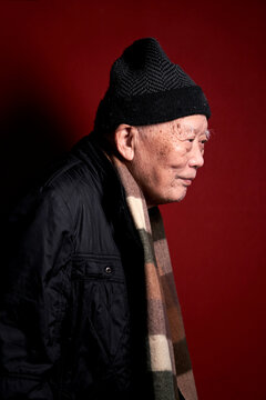 An elderly Chinese man in his seventies at home with a red background
