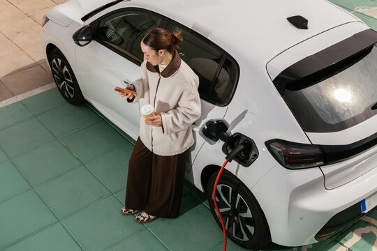 Woman checking smartphone during electric car charging
