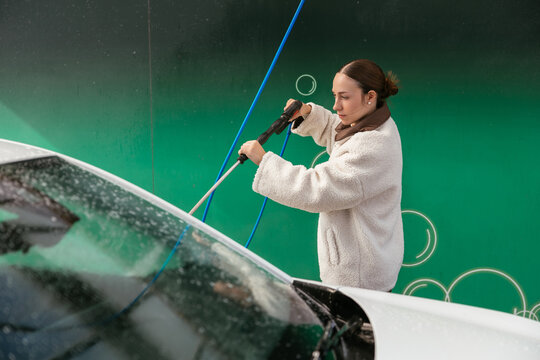 Woman washing white car with pressure washer
