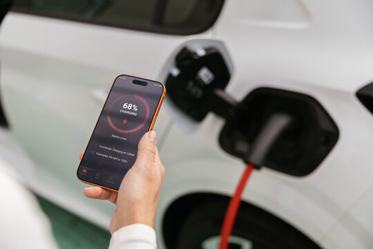 Person holding smartphone monitoring electric car charging status