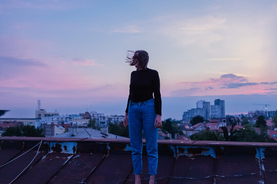 Woman standing on rooftop with windblown hair at dusk