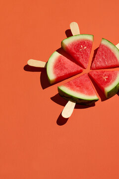 Watermelon popsicles arranged in a circular pattern on orange