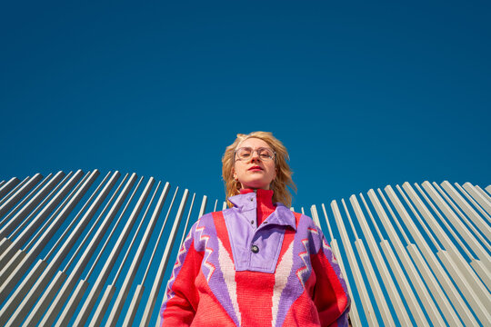 Confident woman in colorful sweater against blue sky and columns