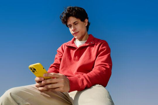 Man using smartphone outdoors sitting under blue sky