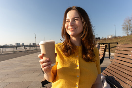 Woman Laughing with Takeaway Coffee on Sunny Park Bench Outdoors