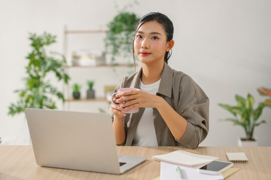 Young Asian woman working on laptop and holding a mug of coffee