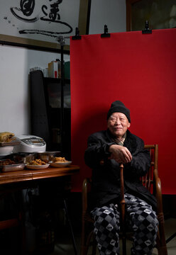 An elderly Chinese man in his seventies at home with a red background