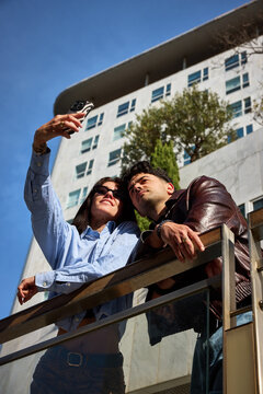 Couple takes selfie on balcony in city under clear blue sky