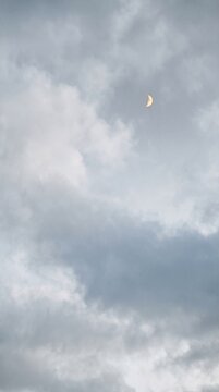 Crescent moon surrounded by soft gray clouds in a moody evening sky