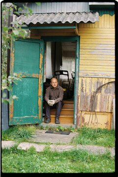 A man is sitting on the porch of a wooden house.