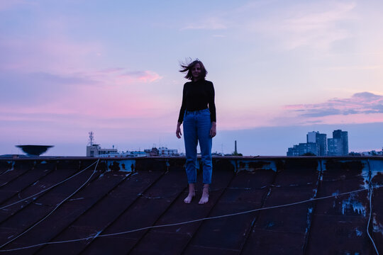 Woman standing barefoot on rooftop at dusk
