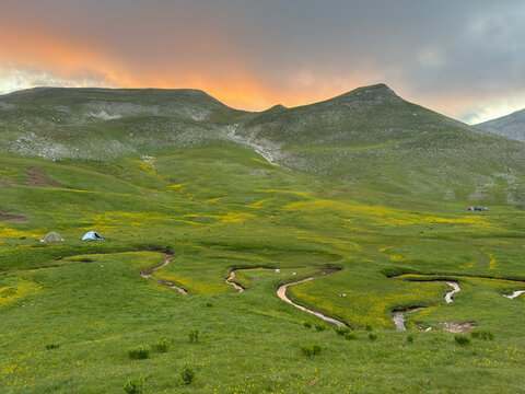 Camping tents in green mountain meadow at sunset