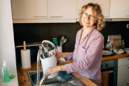 Woman Filling a Kettle in a Kitchen Sink During Daytime