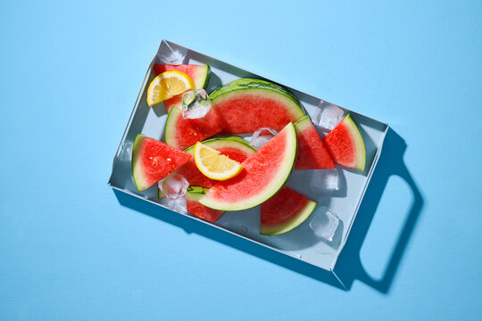 Watermelon slices, lemon, and ice on a blue background