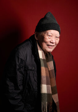 An elderly Chinese man in his seventies at home with a red background