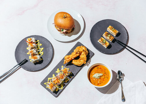Group shot of vegan burger, sushi and soup on a pale pink background