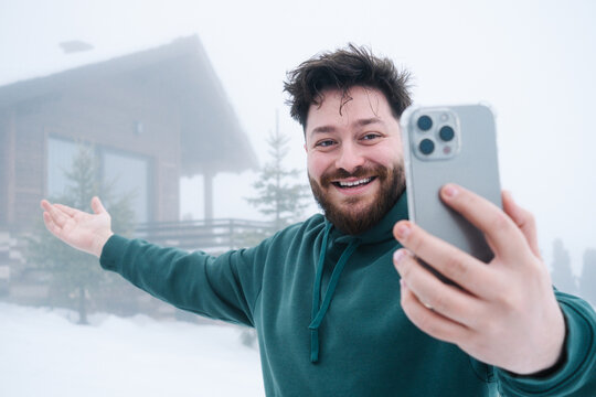 Smiling man on video call outside snowy mountain cabin