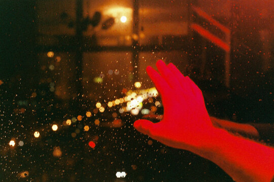 Hand reaching toward rainy window with city lights at night