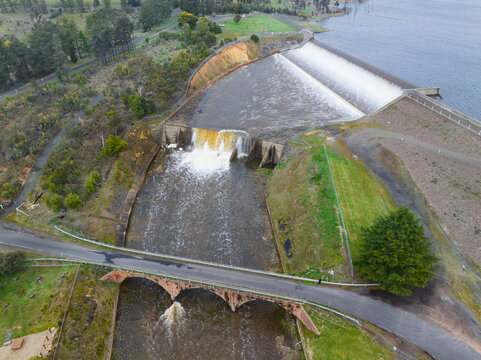 Arched road bridge crossing water rushing over a reservoir spillway