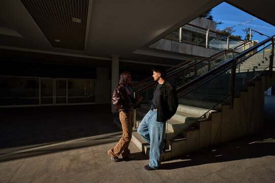 Two people talk in a building with stairs and light in the eveni