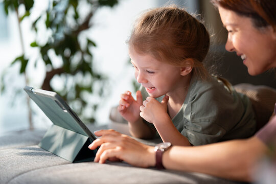 Child and adult have fun with tablet on couch