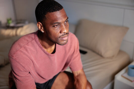 Thoughtful man sitting on bed gazing out window in morning light
