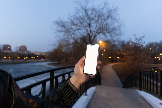 Hand Holding Smartphone with Blank Screen on Bridge at Dusk in Park
