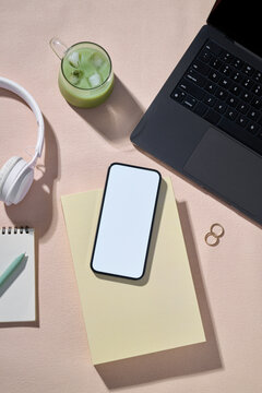 A workspace setup with a laptop, matcha drink and a blank screen phone
