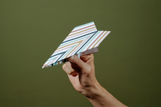 a man holds a striped paper airplane against a green background