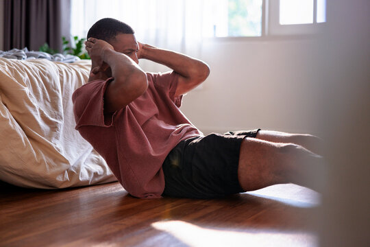 Man doing sit-ups on floor in bedroom.