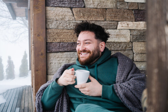 Smiling man with hot drink on terrace of mountain cabin