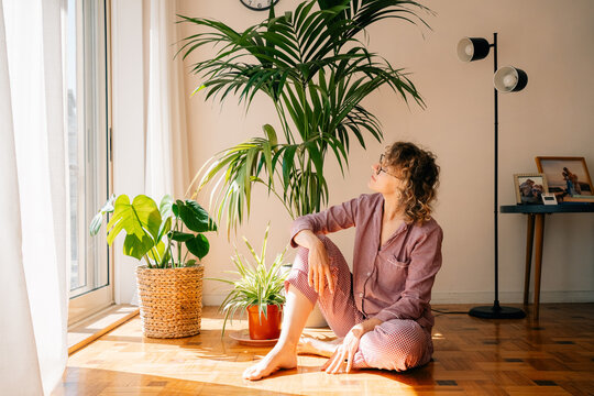 Woman Sitting on Floor With Plants and Sunlight in Home Space